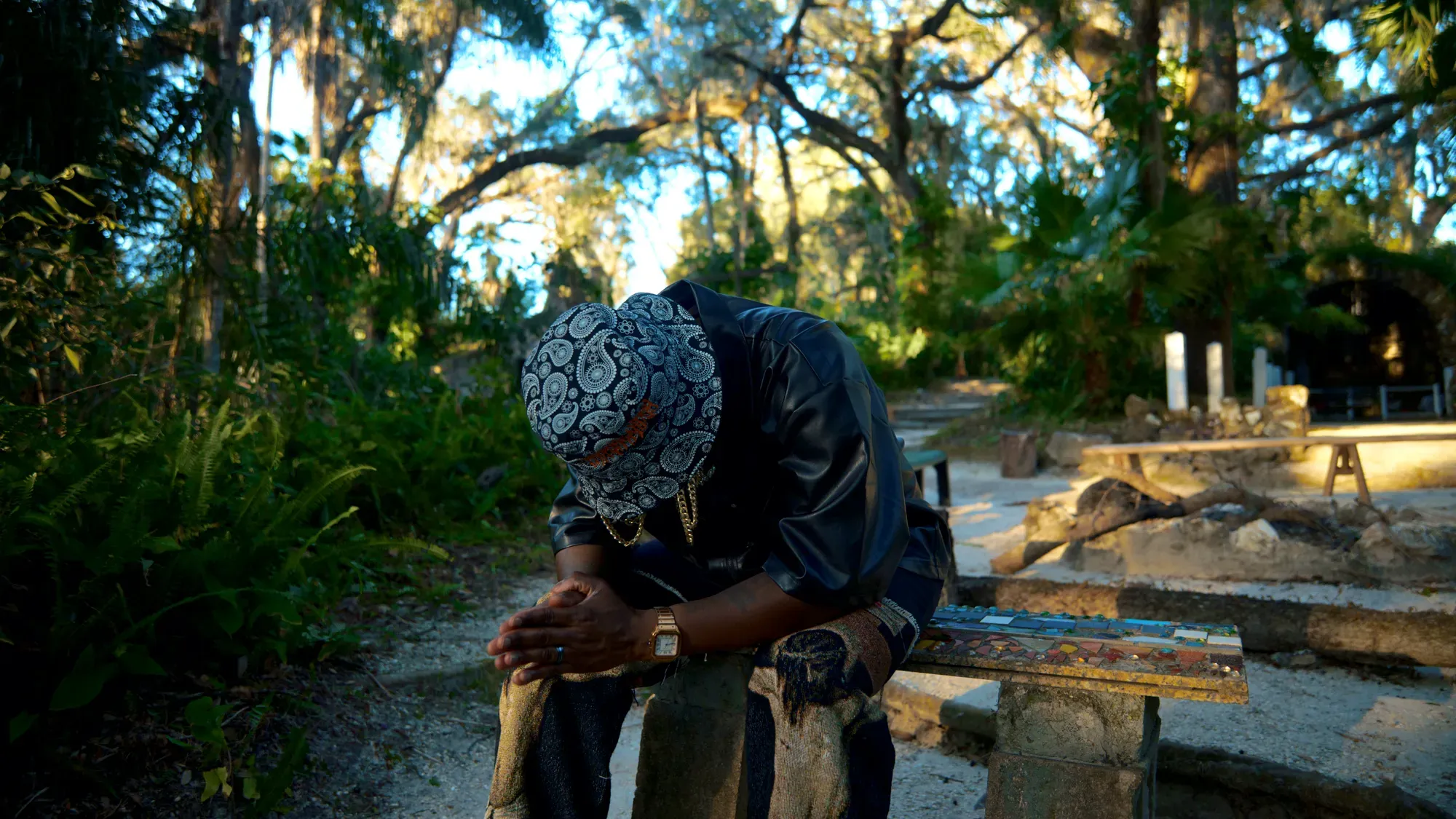 Pusha Preme seated with his head bowed and hands clasped.