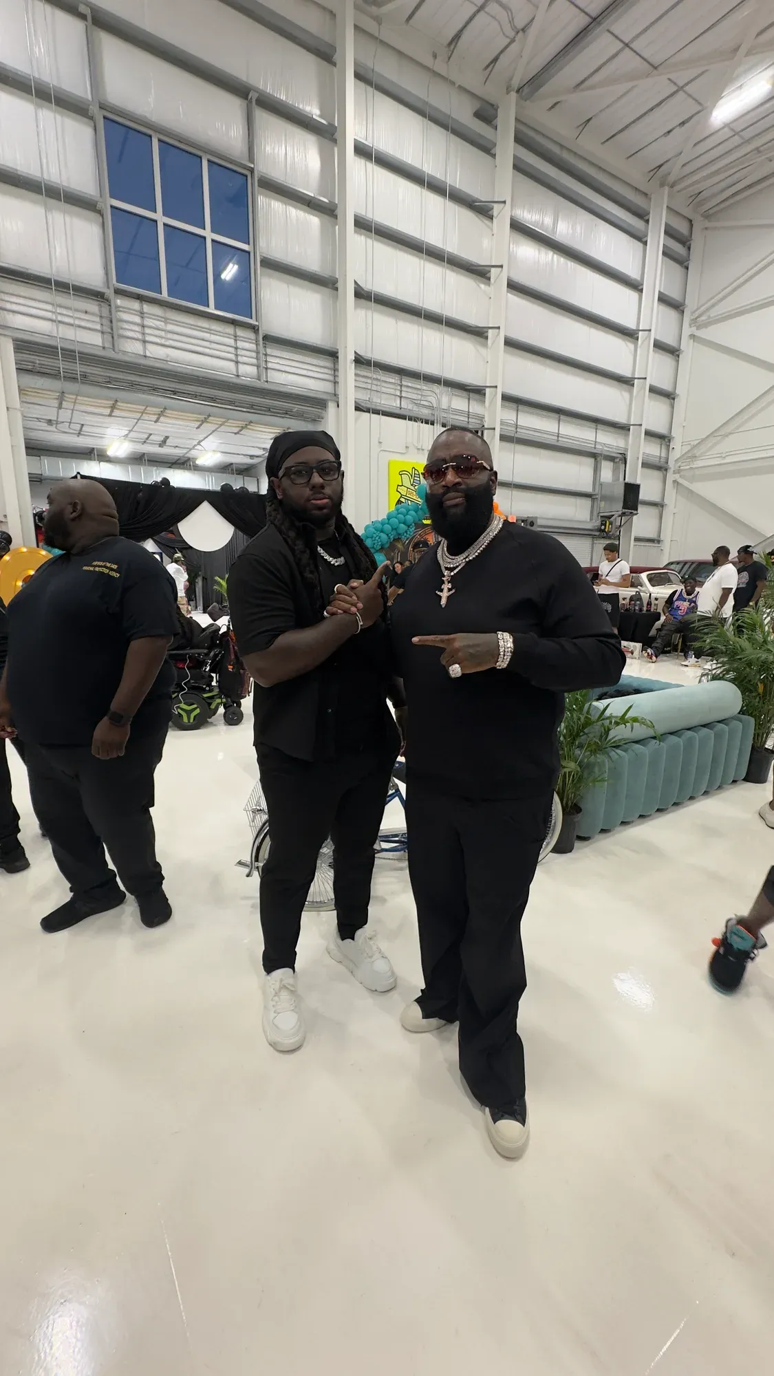 Rick Ross and another man clasping hands in a large event space.