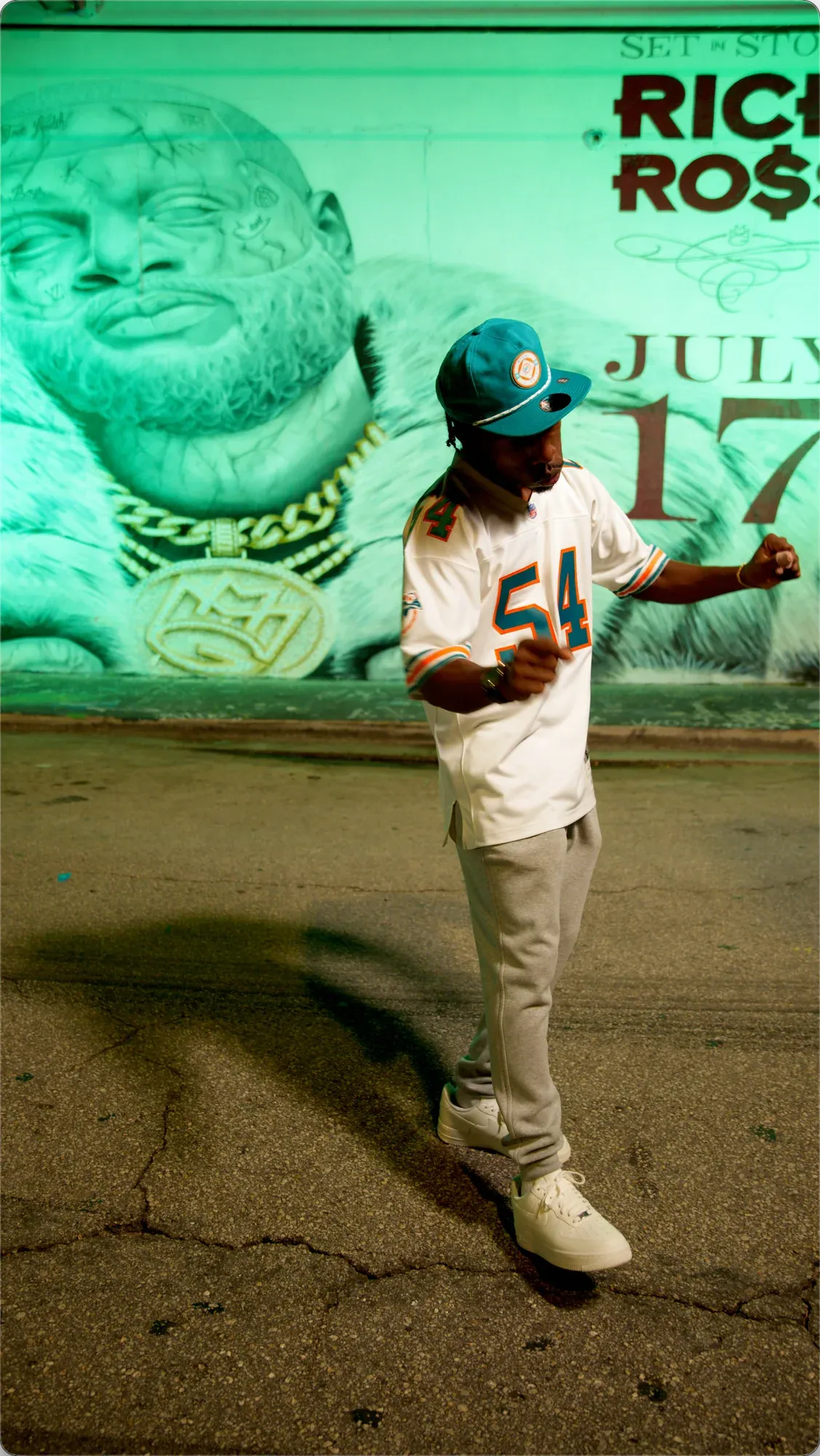 INIKIO performing full length in a #54 jersey in front of the green-lit Rick Ross mural and July 17 lettering.