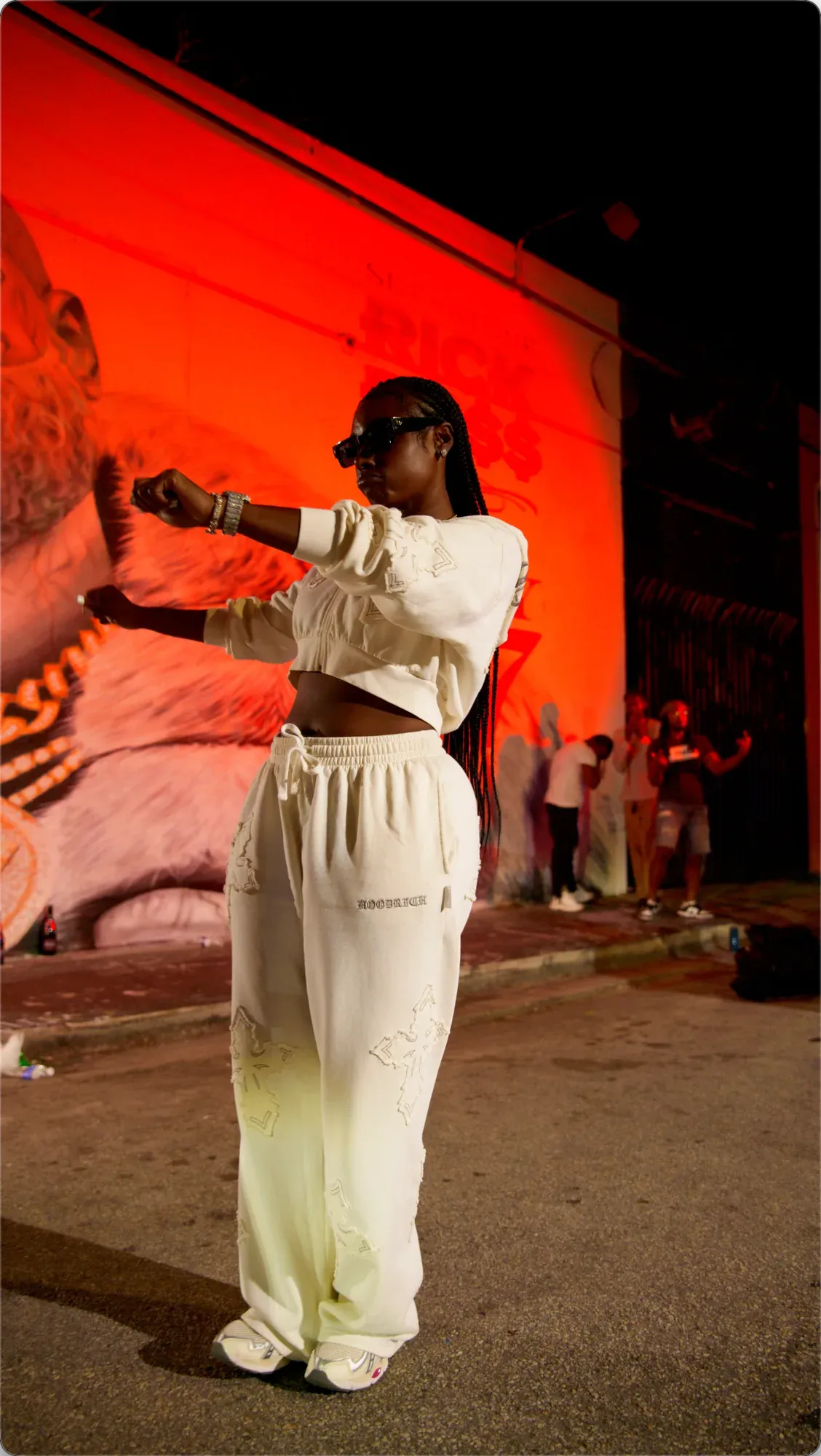 VSTUCK standing full length in front of the Rick Ross mural and its lettering at night.